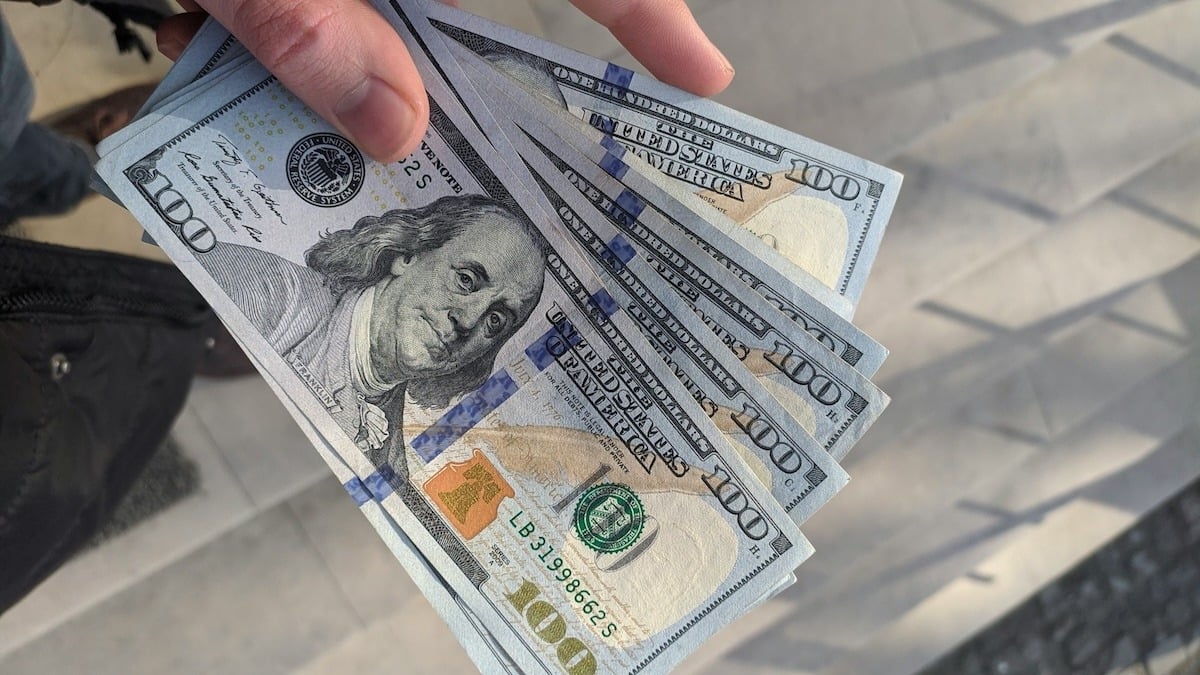 Person holding a stack of $100 bills to give as a holiday tip