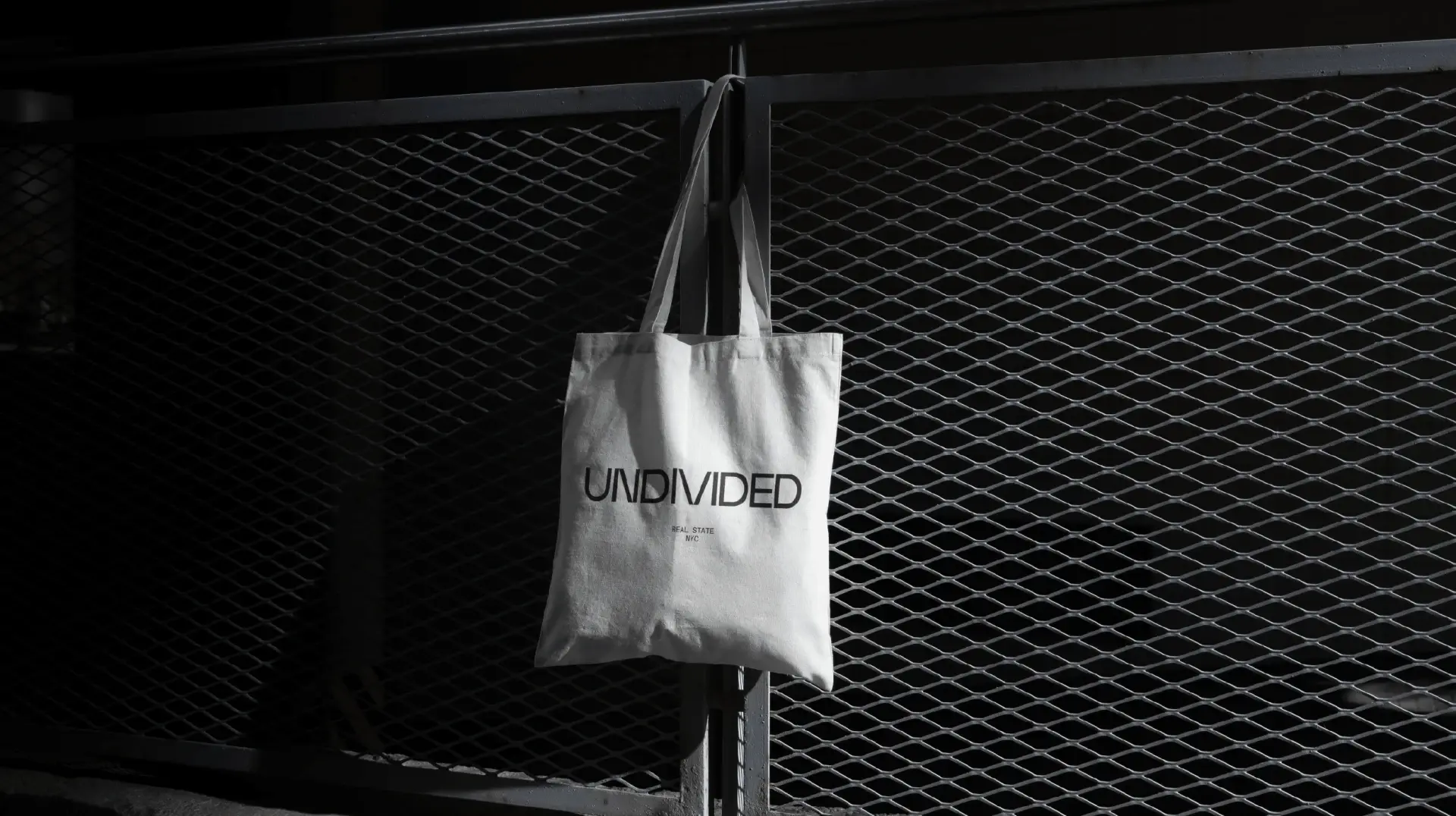 Black and white Undivided tote bag hanging against an industrial metal backdrop.