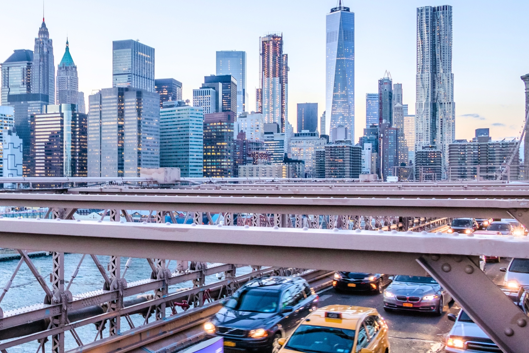 A view from the Brooklyn Bridge showing cars, taxis, and Manhattan skyscrapers.