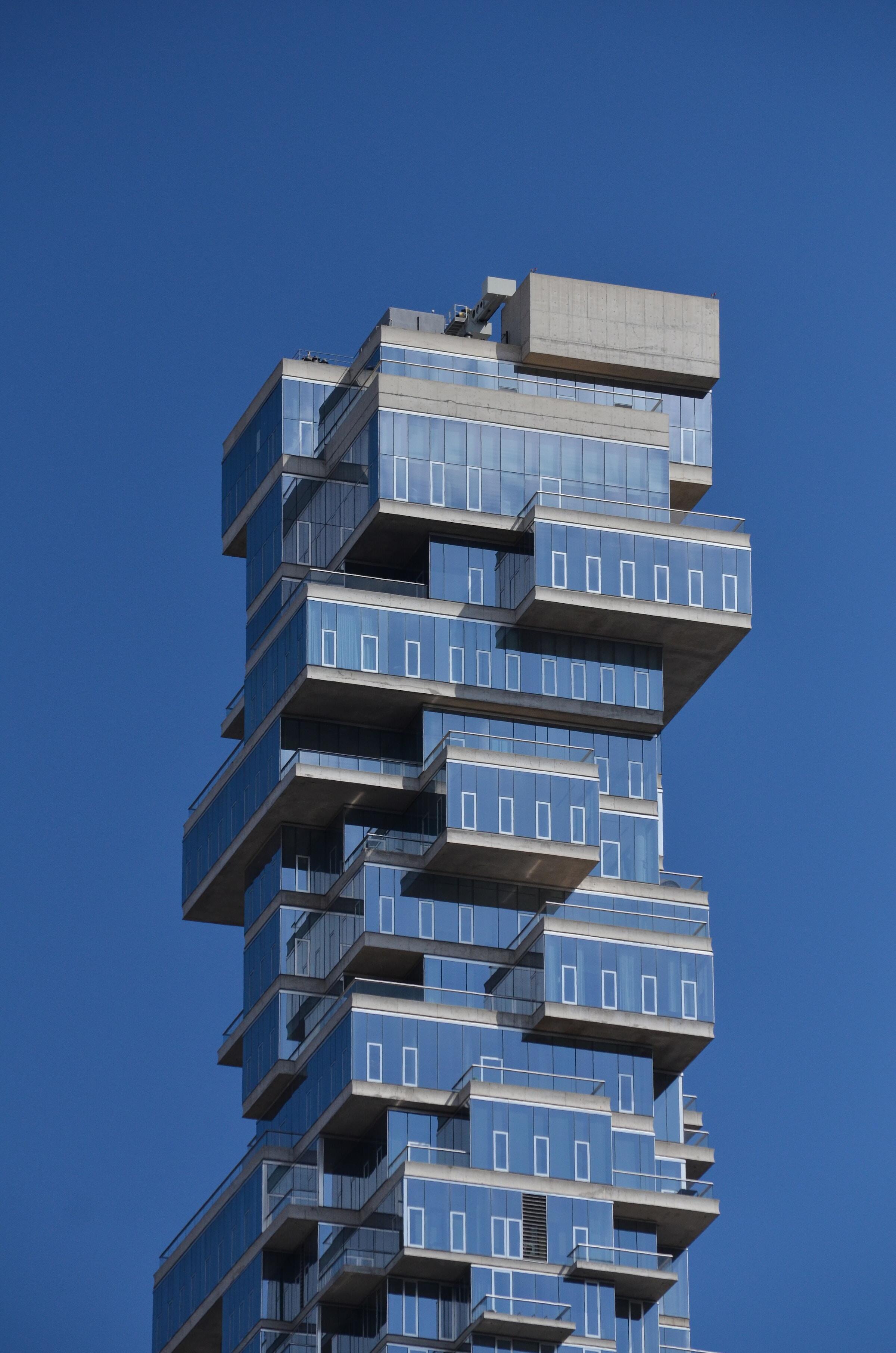 Modern high-rise building with stacked glass balconies against a blue sky, highlighting innovative urban architecture.