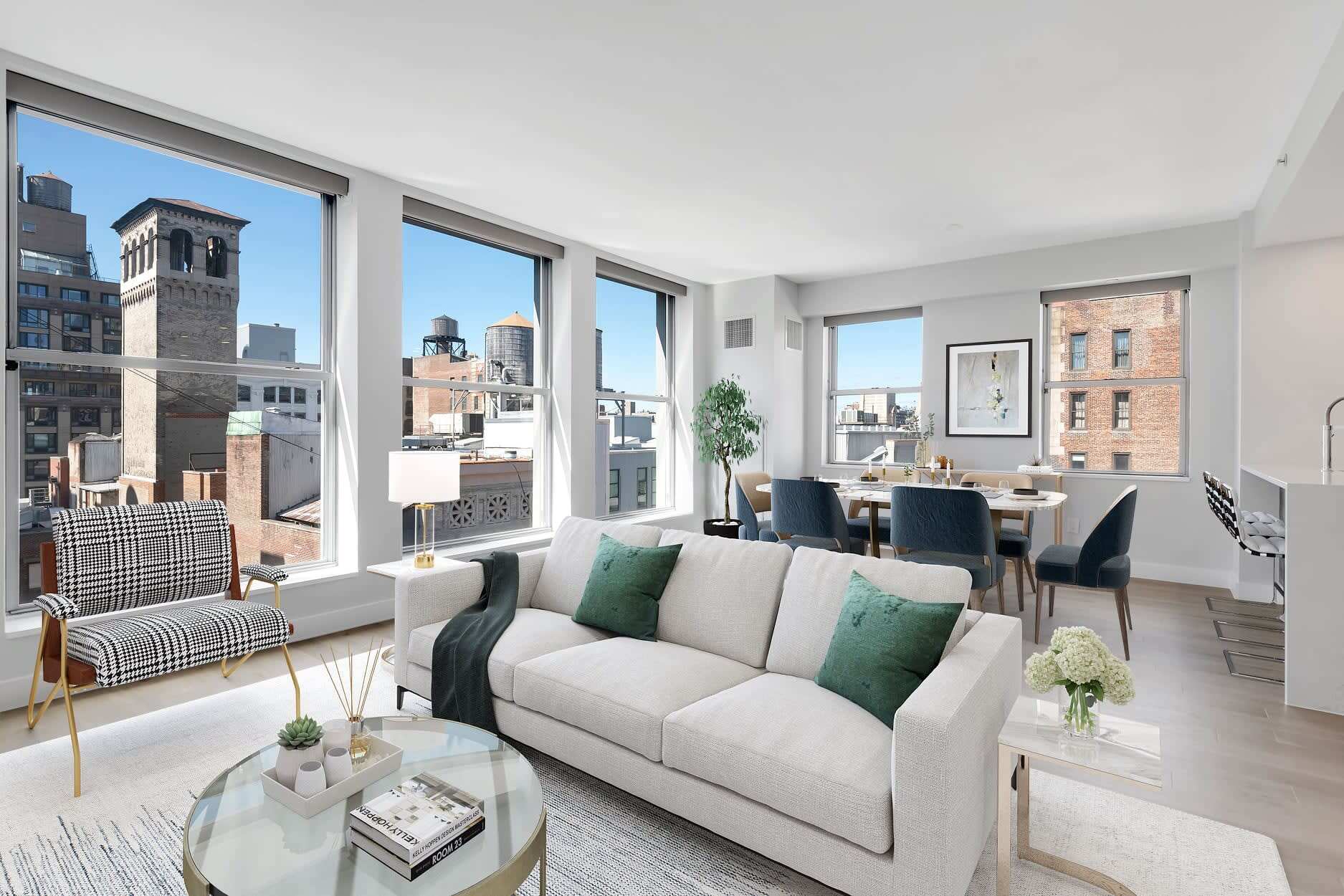 A spacious living room with large windows, modern decor, and a city skyline backdrop.