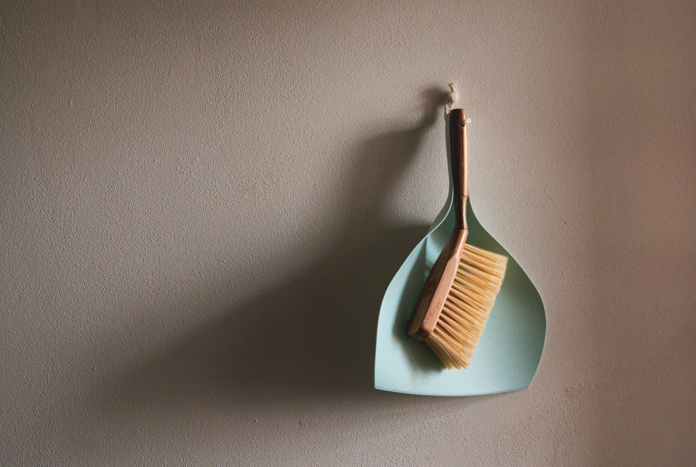 A hanging dustpan and brush set against a neutral wall, emphasizing home maintenance and cleanliness.