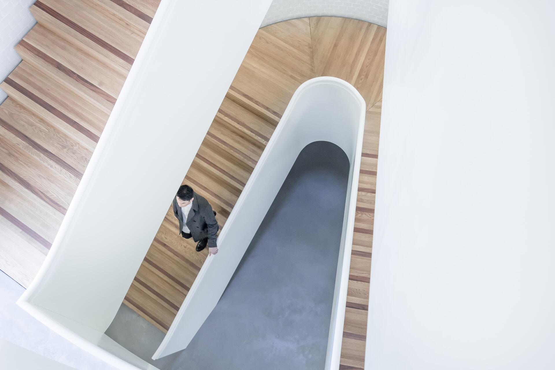 A man walking on a contemporary white staircase with wooden steps, depicting architectural elegance.