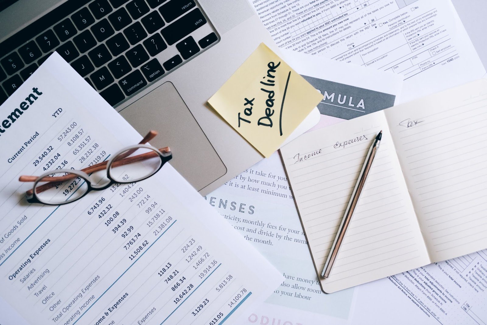 Tax papers stacked on desk with Apple Macbook and post-it note