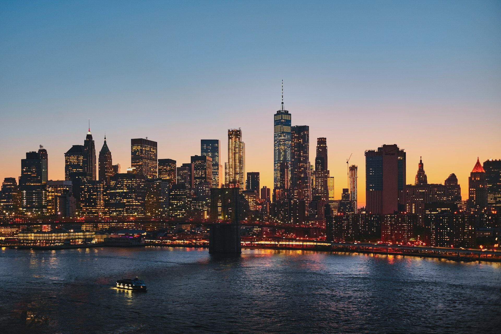 New York City skyline at dusk with illuminated skyscrapers over the East River.