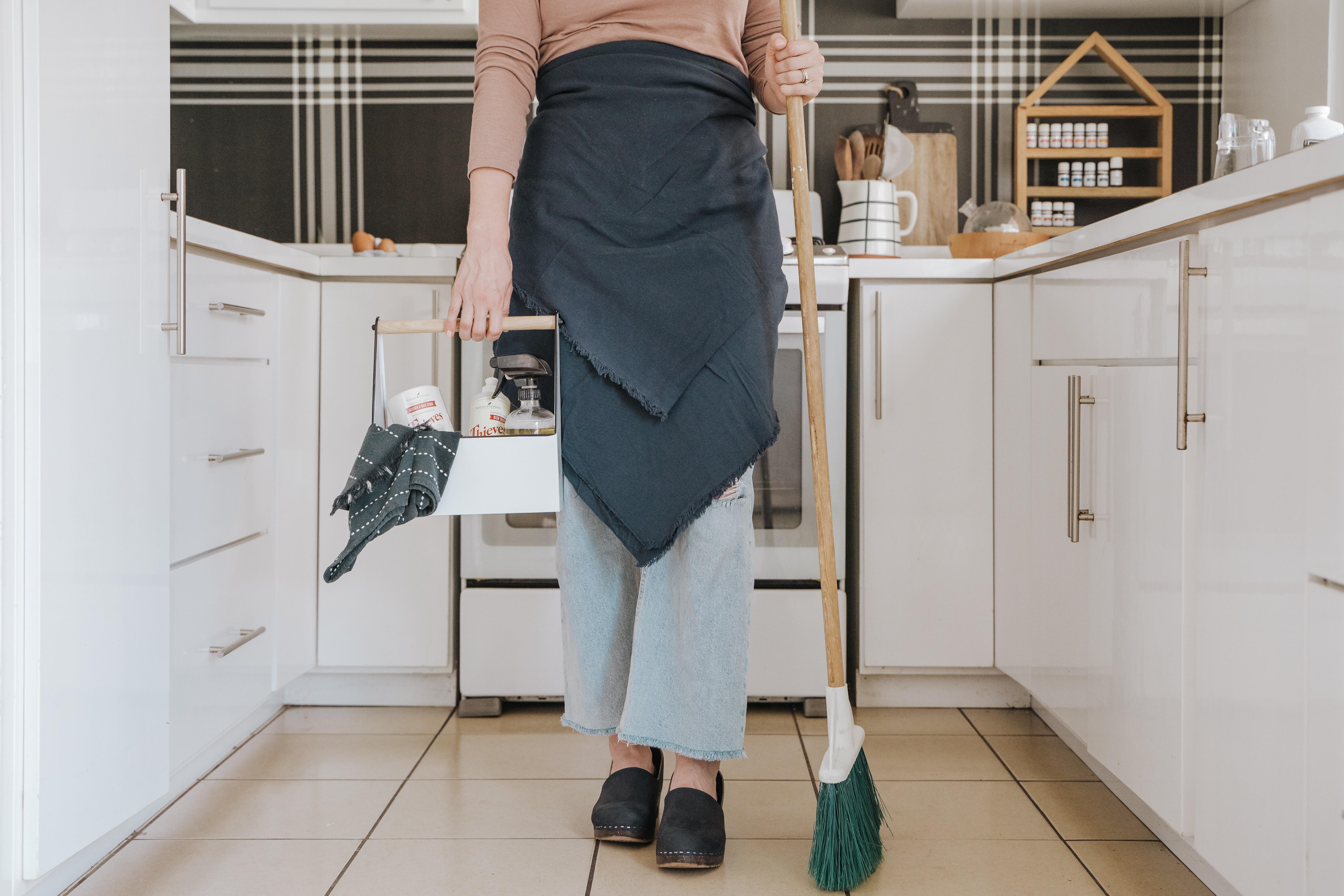 Woman with broom and cleaning supplies standing in a kitchen